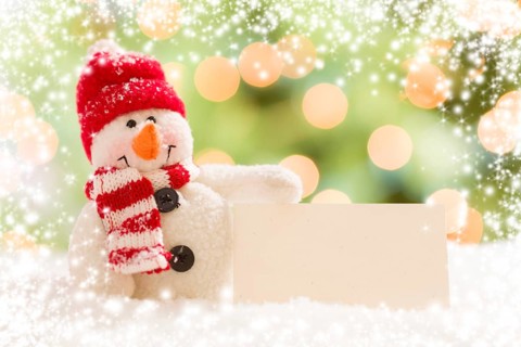 Cute snowman with scarf and hat next to blank white card over abstract snow and light background
