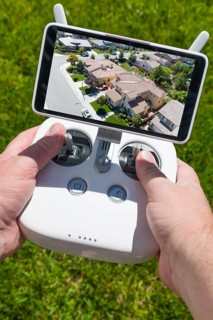 Hands holding drone quadcopter controller with residential homes on screen