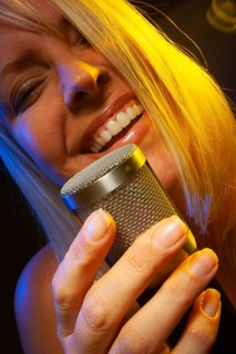 Female vocalist under gelled lighting sings with passion into condenser microphone