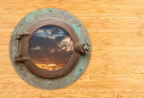 Antique porthole with view of sunset on a bamboo wall background