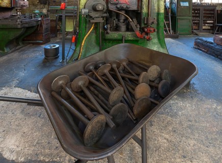 Car valves in the raw state in a wheelbarrow in front of a screw press in a drop forge