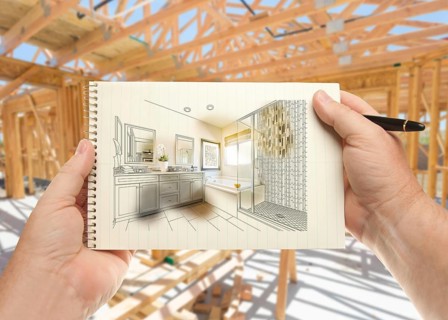 Hands holding pen and pad of paper with bathroom design inside house construction framing