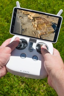 Hands holding drone quadcopter controller with construction house framing on screen