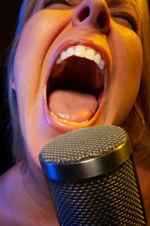 Female vocalist under gelled lighting sings with passion into condenser microphone