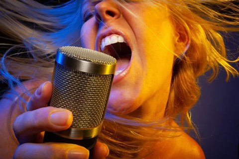 Female vocalist under gelled lighting sings with passion into condenser microphone
