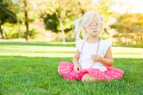 Cute little girl playing dress in the grass up with pink glasses and beaded necklace