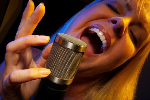 Female vocalist under gelled lighting sings with passion into condenser microphone