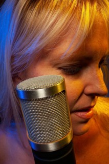Female vocalist under gelled lighting sings with passion into condenser microphone