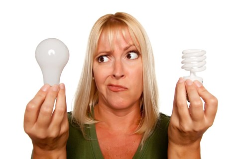 Funny faced woman holds energy saving and regular light bulbs isolated on a white background