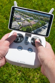 Hands holding drone quadcopter controller with residential homes on screen