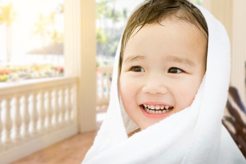 Happy cute mixed-race chinese and caucasian boy on tropical patio wrapped in A towel