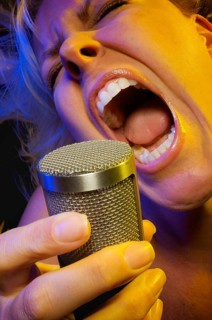 Female vocalist under gelled lighting sings with passion into condenser microphone