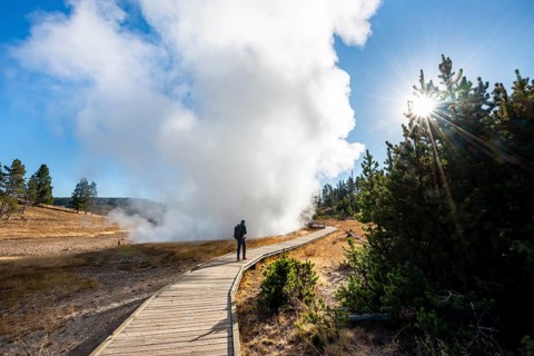 Hiker on footbridge next to steaming hot spring
