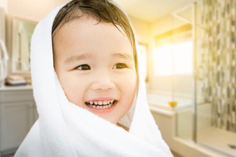 Happy cute mixed-race chinese and caucasian boy in bathroom wrapped in A towel