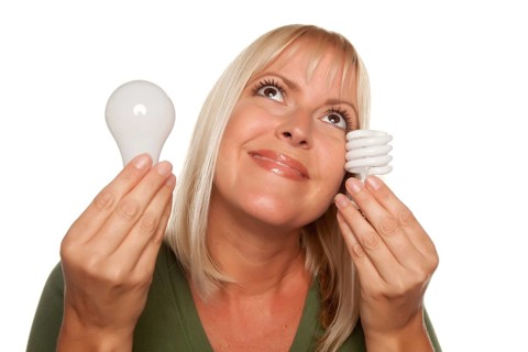Smiling woman holds energy saving and regular light bulbs isolated on a white background