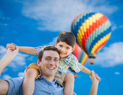 Father and son playing piggyback with hot air balloons floating behind them