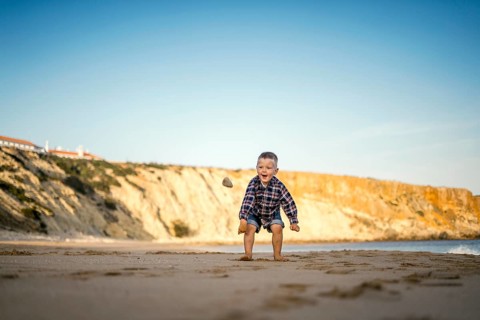 Small boy throwing stones on the beach by the sunset