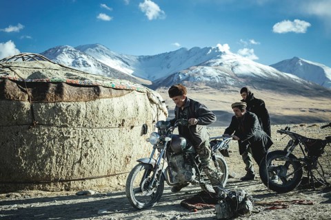 Two men push the motorcycle of a Kyrgyz nomad to get it running again