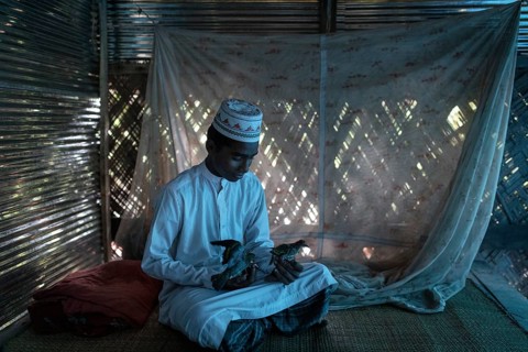 Ahmed on a raffia rug on the floor of a hut playing with two birds