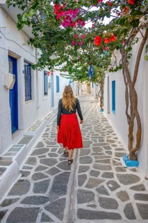 Young woman with dress walking through alley with Cycladic houses