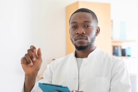 Young black doctor with smock and tablet explaining in the surgery