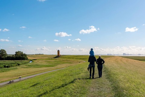 Young family walking on the high water dam near the Pilsum lighthouse