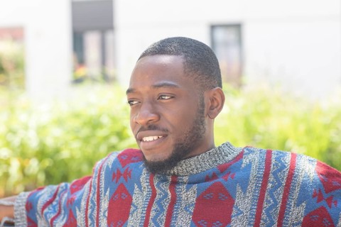 Young black man sitting on bench with African poncho