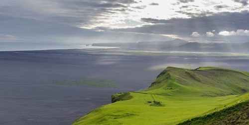 Old farmstead at Hjoerleifshoefdi (Viking grave) behind wide lava sand area and the Reynisdrangar