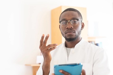Young black doctor with smock and tablet explaining in the surgery