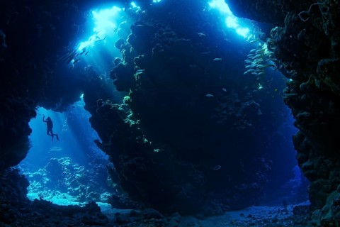 Sunbeams shining through reef top in cave in coral reef with diver