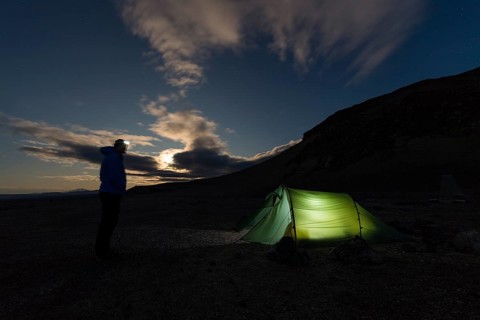 Man with headlamp standing in front of tent lit from inside