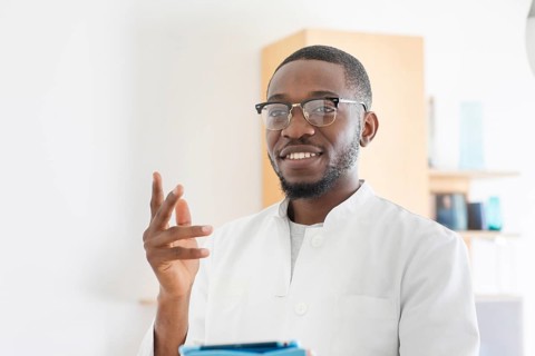 Young black doctor with smock and tablet explaining in the surgery