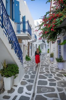 Young woman with dress walking through alley with Cycladic houses