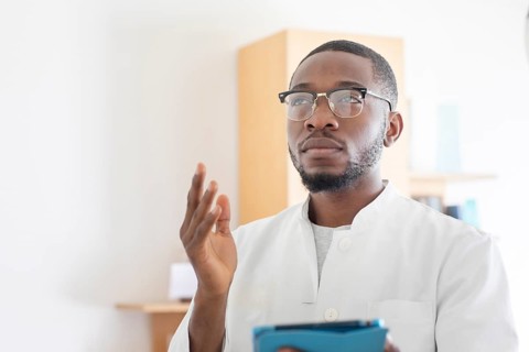 Young black doctor with smock and tablet explaining in the surgery
