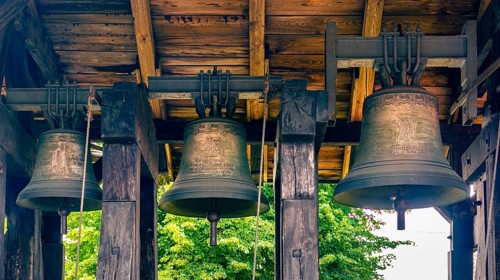 A belfry standing on the ground with four bells of different sizes in the village of Miloradz