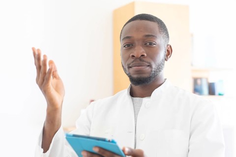 Young black doctor with smock and tablet explaining in the surgery