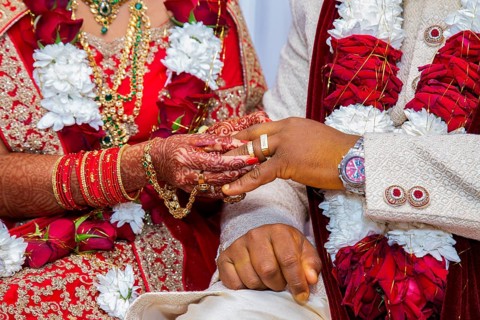 Bride with bridal jewelry and henna decoration on her hand attaches ring to the groom's finger at traditional religious ceremony at a Hindu wedding