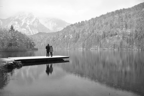 Lake with reflection and footbridge with two people in winter black and white