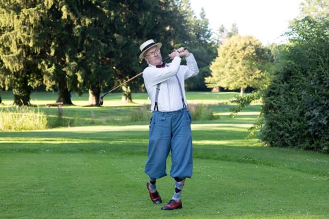 Older man in straw hat and knickerbockers playing hickory golf on a golf course