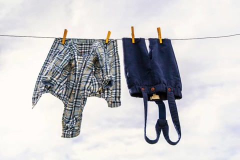 Elegant baby trousers and shirt pinned with wooden pegs against cloudy sky