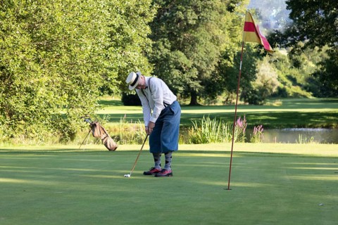 Older man in straw hat and knickerbockers playing hickory golf on a golf course