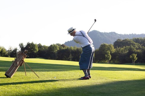 Older man in straw hat and knickerbockers playing hickory golf on a golf course
