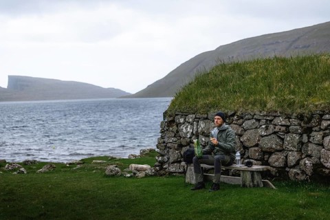 Hiker eating biscuits on a bench in front of a stone hut
