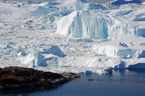Small fishing boat in front of huge icebergs