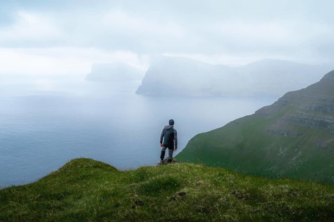 Person standing on the mountain looking at the village of Mikladalur