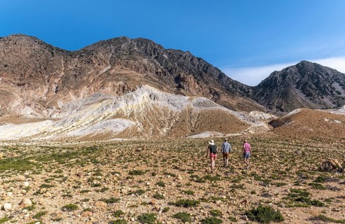 Three tourists hiking in a volcanic caldera with pumice fields
