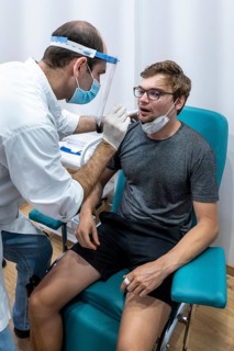 Doctor in protective clothing does an antigen test on a young man