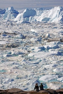 People sitting in front of fjord covered with ice and icebergs