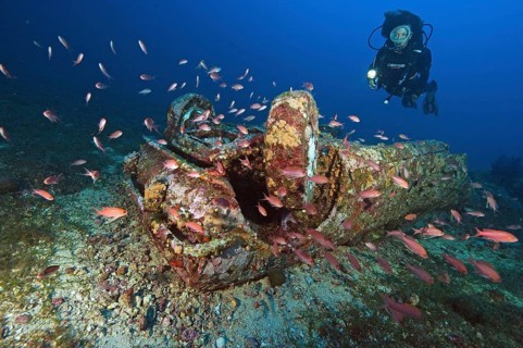 Diver looks at car wreck under water