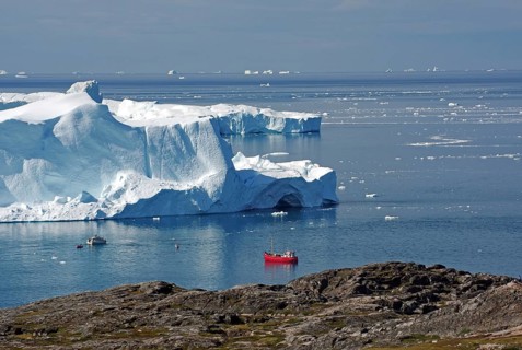 Red fishing boat in a bay with huge icebergs
